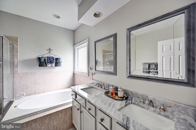 bathroom featuring a relaxing tiled tub, double vanity, and a shower