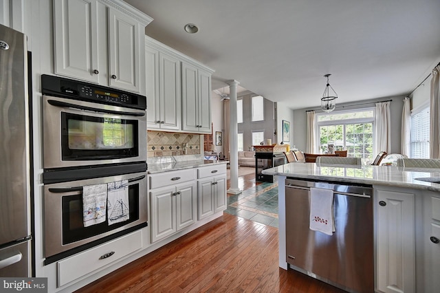 kitchen featuring stainless steel appliances, decorative columns, decorative backsplash, white cabinetry, and recessed lighting