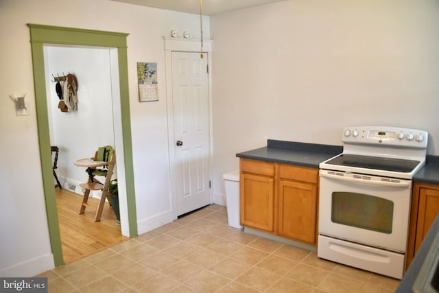 kitchen with white electric range, dark countertops, brown cabinetry, and baseboards