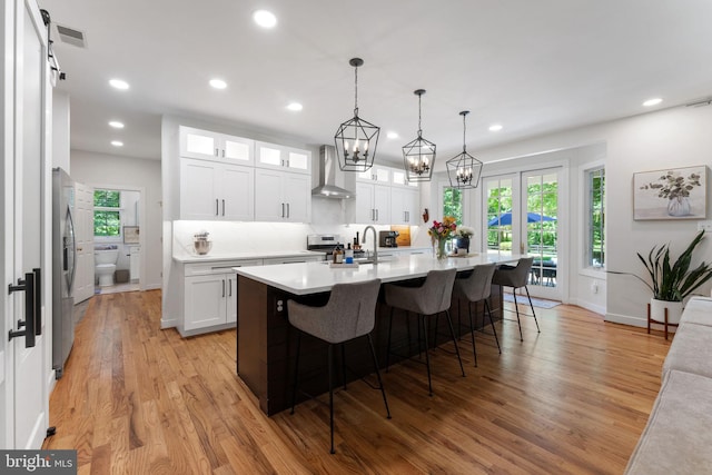 5194 Chase Ln, Midland, VA 22728 - kitchen with wall chimney range hood, light countertops, a kitchen bar, light wood-style floors, and white cabinets