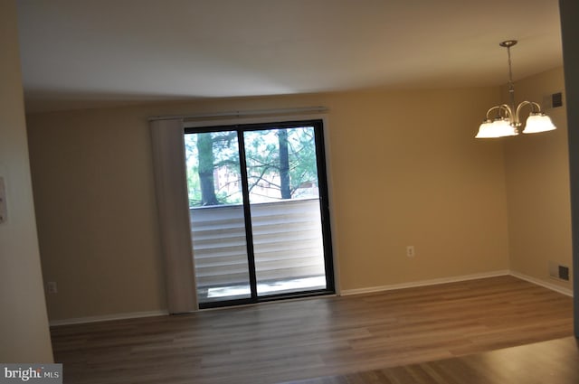 empty room with a chandelier, wood finished floors, and baseboards