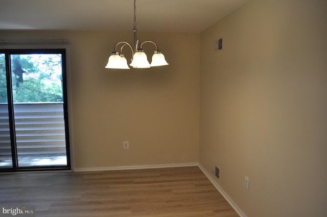 spare room with a chandelier, wood finished floors, and baseboards