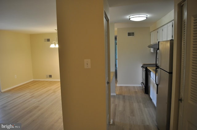 kitchen featuring freestanding refrigerator, under cabinet range hood, electric range, light wood-style floors, and white cabinets