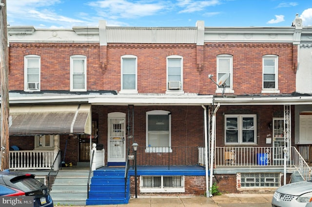 townhome / multi-family property with a porch, brick siding, and cooling unit