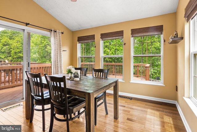 dining area featuring lofted ceiling, light wood-type flooring, baseboards, and a textured ceiling