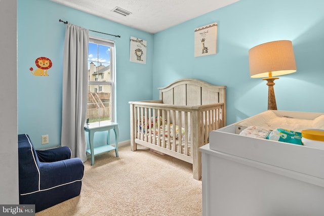 carpeted bedroom featuring a textured ceiling and a nursery area