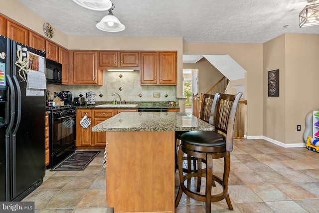 kitchen featuring black appliances, decorative backsplash, baseboards, a sink, and light stone countertops