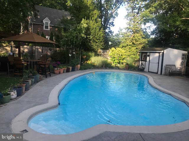 view of pool with a patio area, an outdoor structure, and view of wooded area