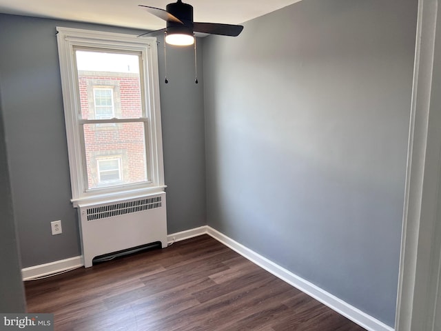 empty room featuring radiator heating unit, ceiling fan, dark wood-type flooring, and baseboards