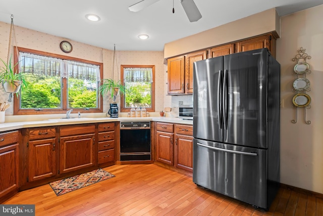 kitchen featuring freestanding refrigerator, dishwasher, a sink, brown cabinets, and light wood-style floors