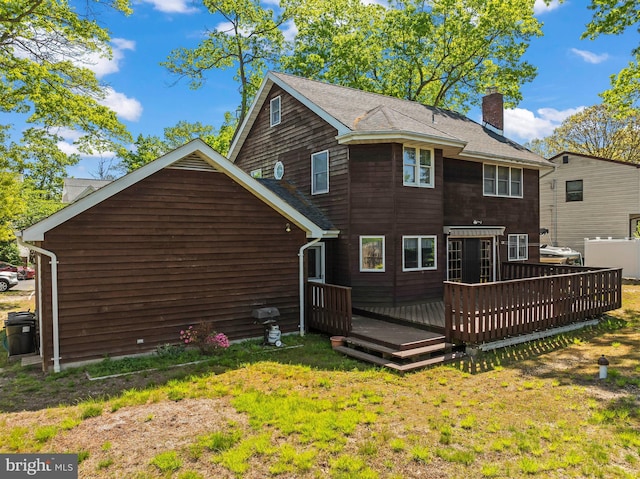 rear view of house with a chimney, a deck, and a lawn