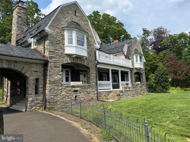view of front of house featuring a balcony, stone siding, a chimney, and a gambrel roof
