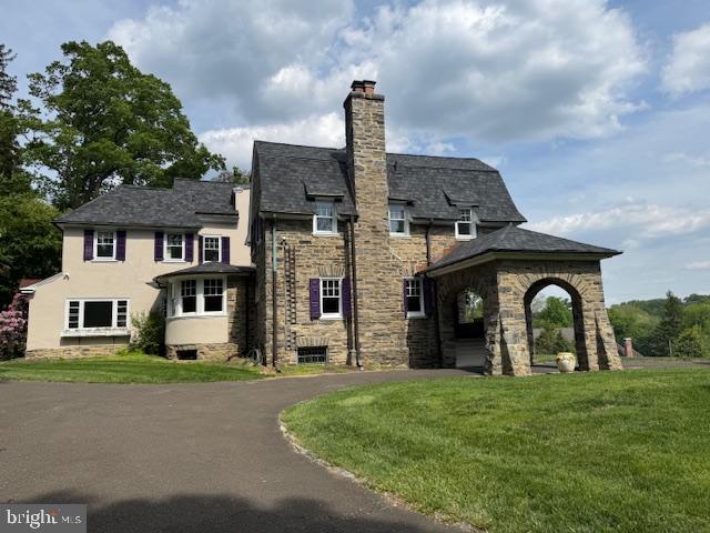 view of side of home featuring a chimney, a yard, stone siding, and asphalt driveway