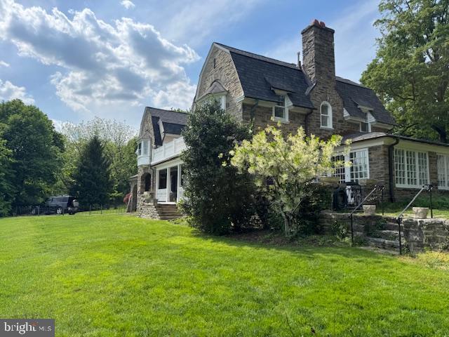 view of side of property featuring stone siding, a chimney, and a yard