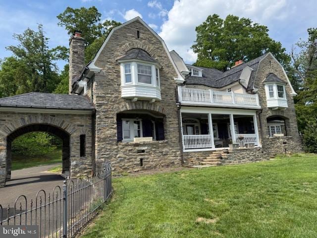 rear view of house featuring a balcony, a chimney, stone siding, and a gambrel roof