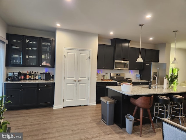 kitchen with appliances with stainless steel finishes, dark cabinetry, a breakfast bar area, glass insert cabinets, and pendant lighting