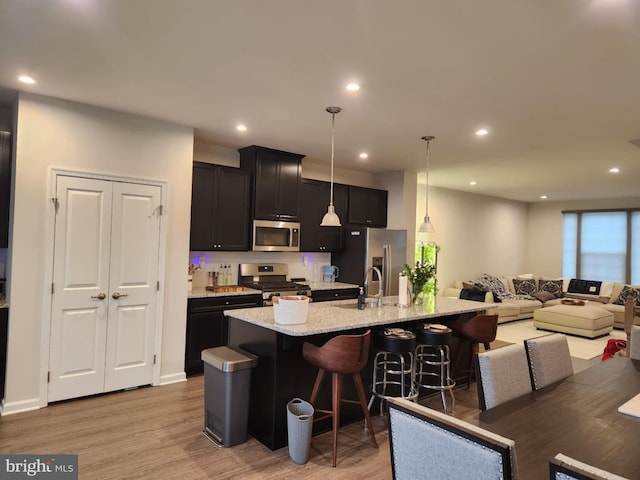 kitchen with stainless steel appliances, a center island with sink, light wood-type flooring, a breakfast bar, and recessed lighting