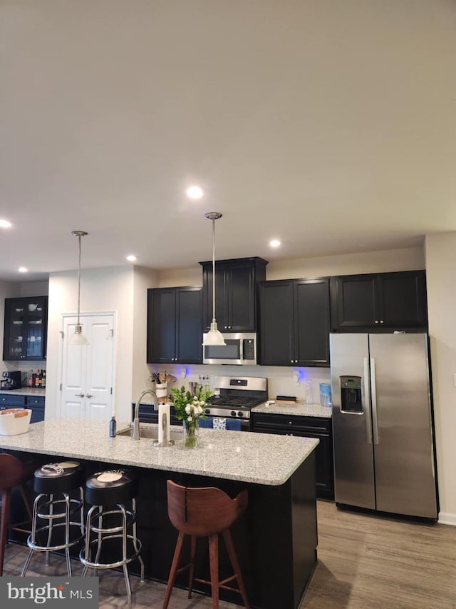 kitchen with stainless steel appliances, a sink, a breakfast bar area, light stone countertops, and recessed lighting