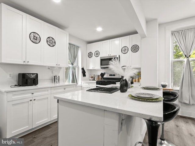 4511 Powell Ave, Baltimore, MD 21206 - kitchen featuring appliances with stainless steel finishes, wood finished floors, white cabinets, a kitchen breakfast bar, and a kitchen island