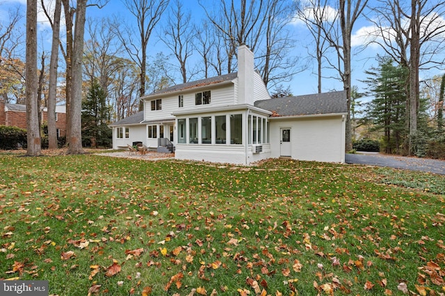 back of property featuring a sunroom, a chimney, a lawn, and a shingled roof