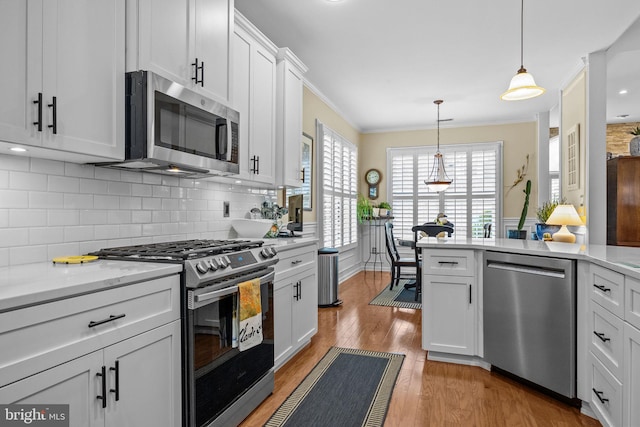kitchen with appliances with stainless steel finishes, light wood-type flooring, backsplash, crown molding, and white cabinetry