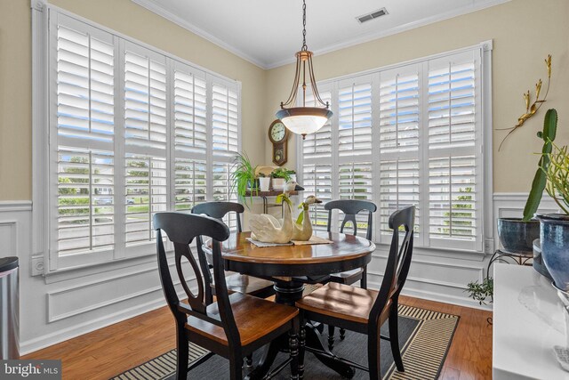dining area featuring wood finished floors, crown molding, a decorative wall, and wainscoting