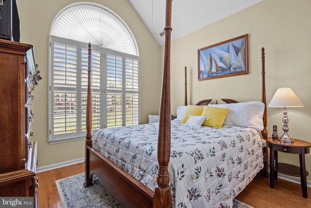bedroom featuring lofted ceiling, multiple windows, wood finished floors, and baseboards