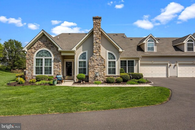 view of front of property with asphalt driveway, roof with shingles, a front yard, stone siding, and a garage