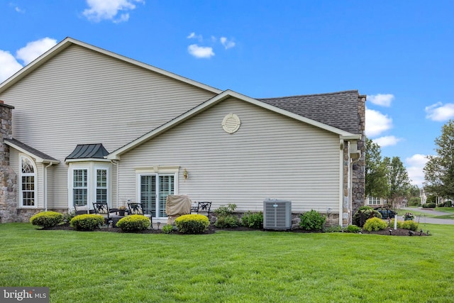 back of property with central AC unit, a yard, and stone siding