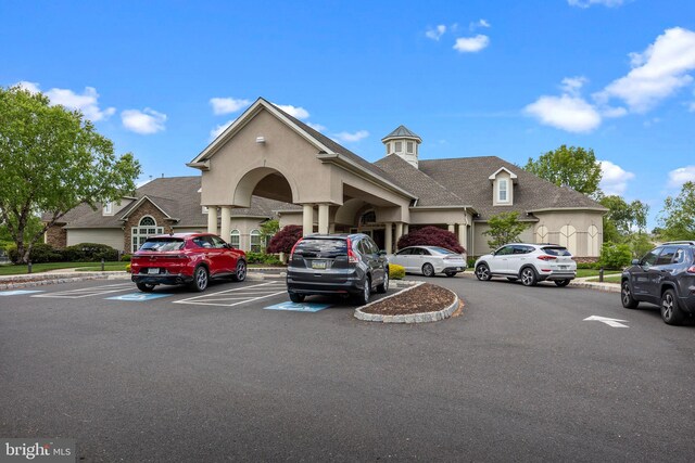 view of front of house featuring uncovered parking, a shingled roof, and stucco siding