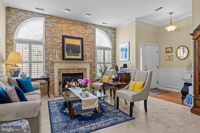 tiled living area featuring a glass covered fireplace, ornamental molding, and wainscoting