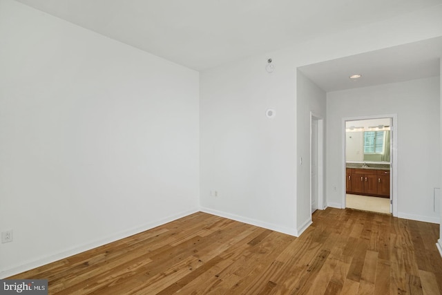 empty room featuring wood-type flooring, a sink, and baseboards