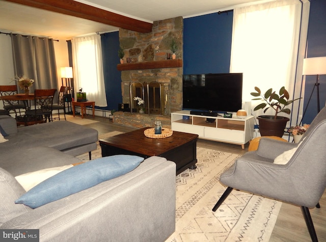 living area featuring wood finished floors, beam ceiling, and a stone fireplace