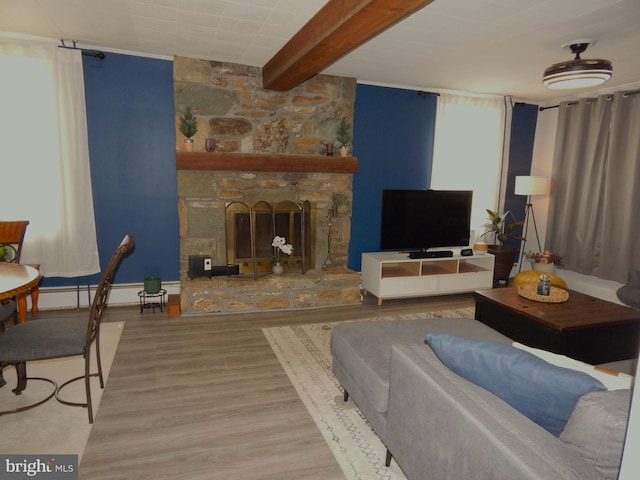 living area with a baseboard heating unit, a stone fireplace, wood finished floors, beam ceiling, and baseboards