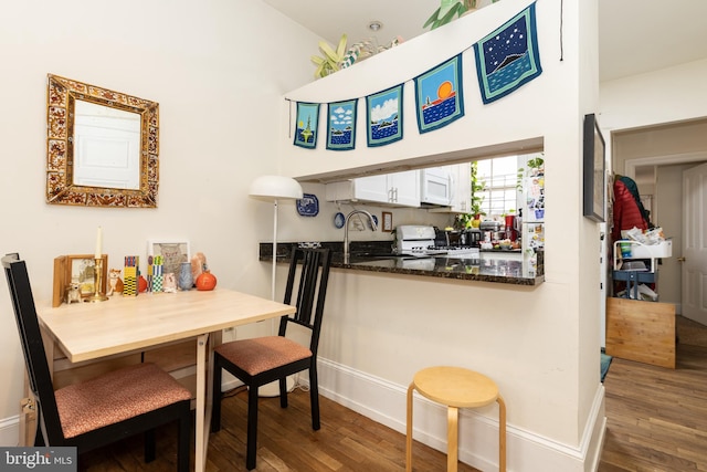kitchen featuring white appliances, wood finished floors, baseboards, and white cabinets
