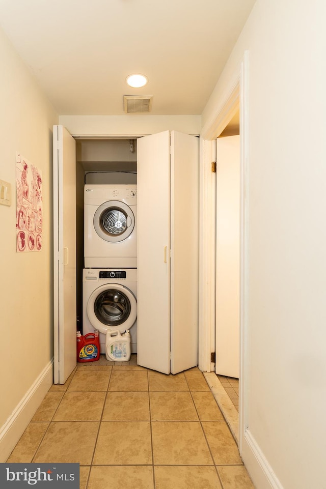 washroom featuring estacked washer and dryer, light tile patterned floors, and baseboards