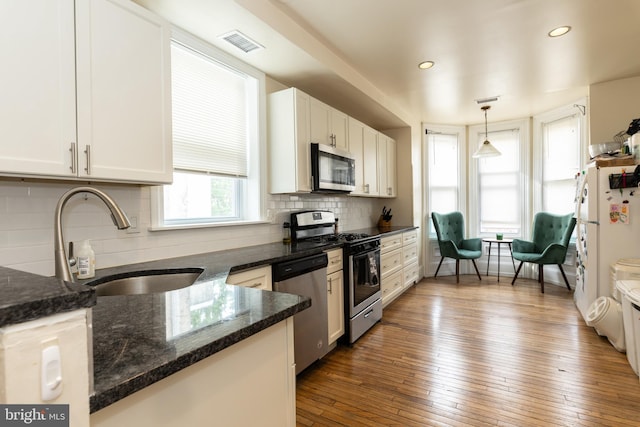 kitchen with stainless steel appliances, a sink, white cabinets, decorative light fixtures, and decorative backsplash