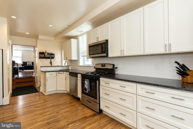kitchen featuring stainless steel appliances, a sink, white cabinetry, light wood-style flooring, and tasteful backsplash