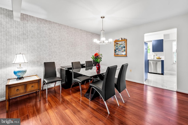 dining area with a chandelier, wood finished floors, wallpapered walls, baseboards, and an accent wall