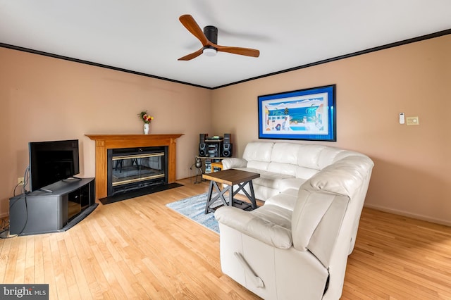 living area featuring ornamental molding, a ceiling fan, hardwood / wood-style flooring, a fireplace with flush hearth, and baseboards