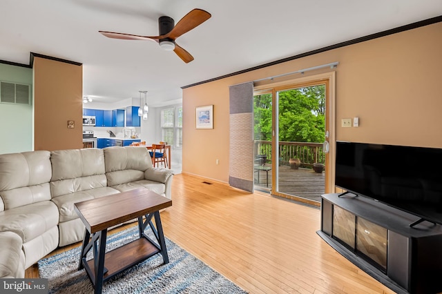 living area featuring a ceiling fan, light wood finished floors, crown molding, and plenty of natural light