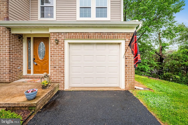 doorway to property with an attached garage, brick siding, and driveway