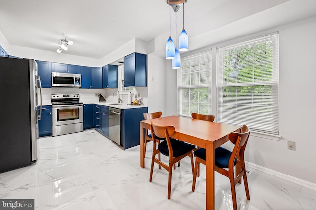 kitchen with appliances with stainless steel finishes, blue cabinets, light marble finish flooring, light countertops, and pendant lighting
