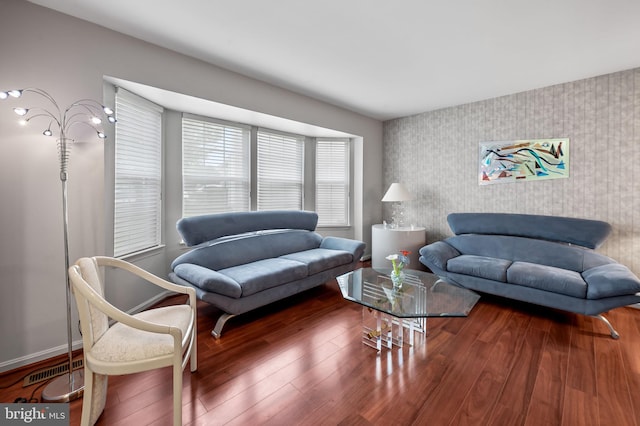 living area with an accent wall, wallpapered walls, wood finished floors, and baseboards