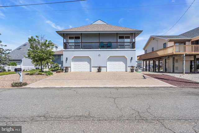 coastal home with an attached garage, a balcony, driveway, and a shingled roof