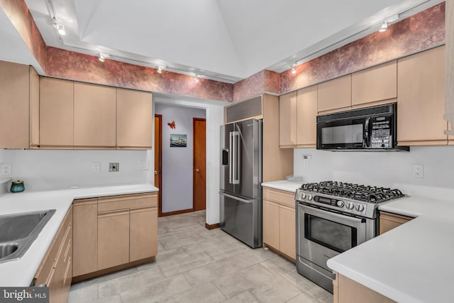 kitchen with appliances with stainless steel finishes, a sink, light countertops, vaulted ceiling, and cream cabinets