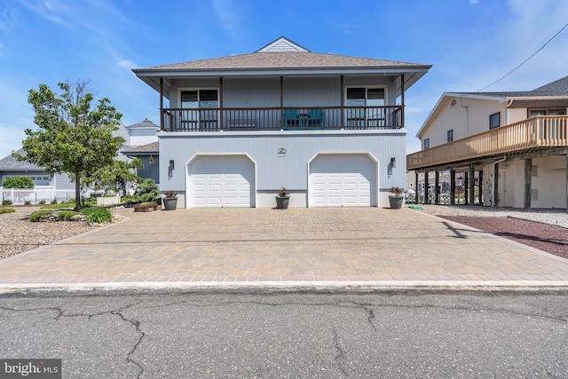 coastal inspired home with decorative driveway, an attached garage, and a balcony