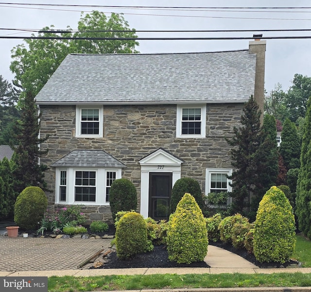 view of front facade with stone siding, a chimney, and a high end roof