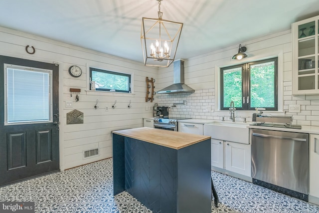 kitchen featuring wall chimney exhaust hood, stainless steel appliances, wood counters, light floors, and a chandelier