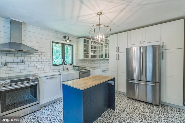 kitchen with appliances with stainless steel finishes, wall chimney exhaust hood, light flooring, decorative backsplash, and glass insert cabinets